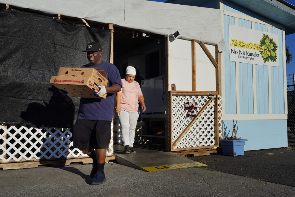 Lahaina Resource & Recovery Center’s LaVatus “Vegas” Donerson, left, carries out strawberries and tomatoes with Etina “Edna” Hingano Thursday, Dec. 19, 2024, in Wailuku. Edna and Vegas both lost their homes and belongings in the Aug. 8, 2023, Lahaina fire. (Kevin Fujii/Civil Beat/2024)