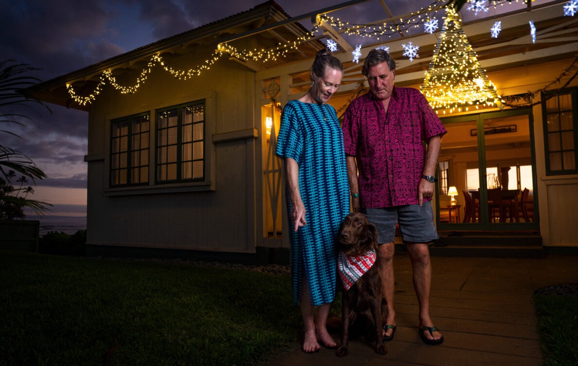 Dora,Trip and Shrimpie Millikin are photographed outside of their “Miracle House” Thursday, Dec. 19, 2024, in Lahaina. The house made it through the Aug. 8, 2023, fire with very little damage. (Kevin Fujii/Civil Beat/2024)