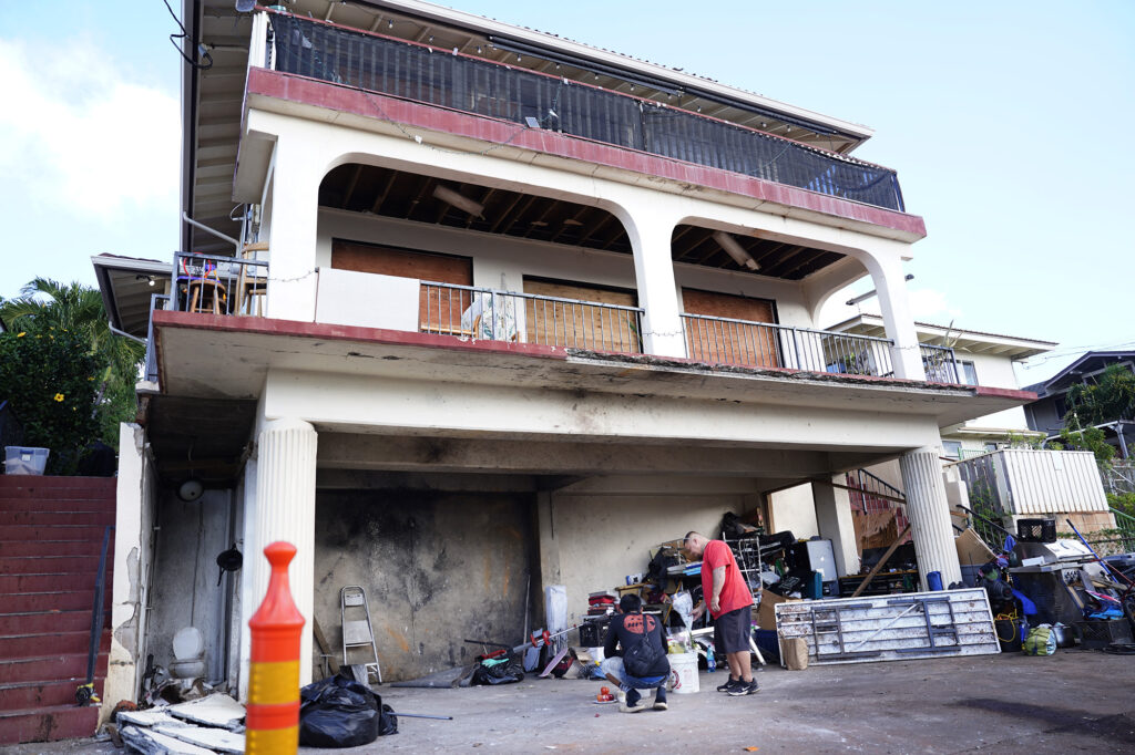 Lance Jordan, right, of Kaneohe, and an unidentified passenger from his truck leave flowers at a home where a deadly, New Year’s Eve fireworks explosion took place Thursday, Jan. 2, 2025, in Honolulu’s Salt Lake neighborhood. Multiple fatalities and injuries were reported. Jordan, 30, grew up on this street but has since moved to Kaneohe. (Kevin Fujii/Civil Beat/2025)