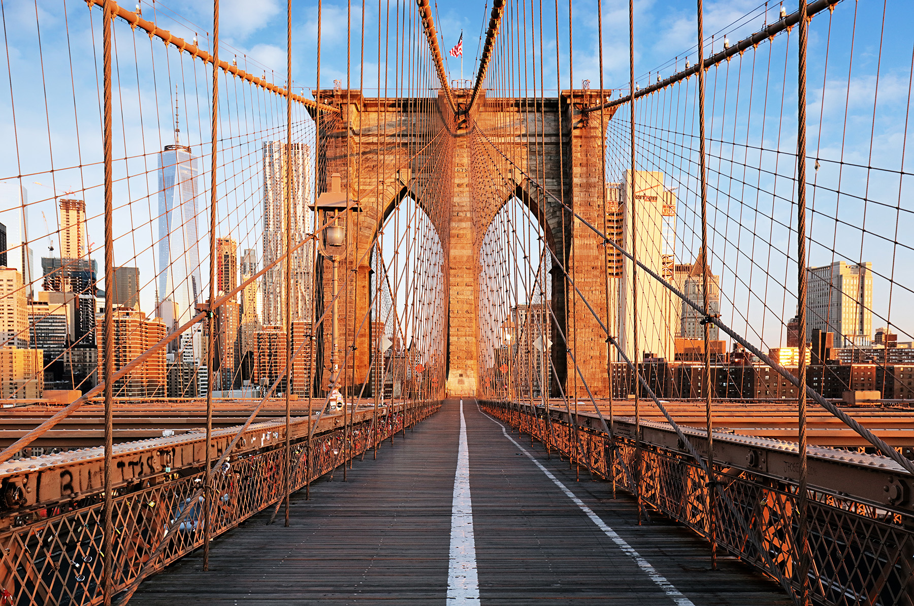 photograph of the pedestrian and bike lanes on a bridge. The steel-wire suspension cables can be seen connecting to one of the bridge towers. The cityscape is in the background.