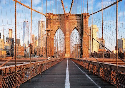 photograph of the pedestrian and bike lanes on a bridge. The steel-wire suspension cables can be seen connecting to one of the bridge towers. The cityscape is in the background.