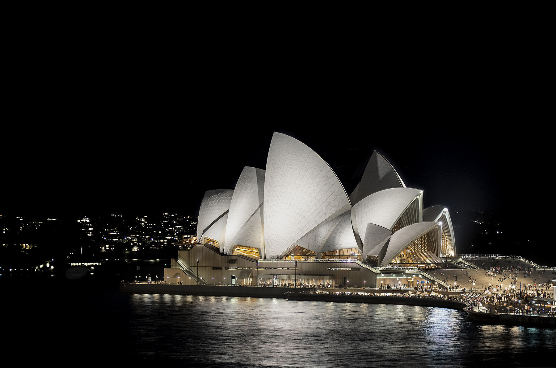 nighttime photo of a structure surrounded by water. People are outside enjoying the venue.