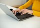 A woman with a gold sweater on types on a laptop. 