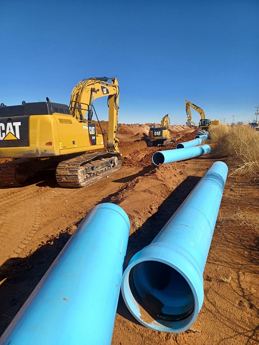 Large blue pipes sit in a field. There is also mechanical equipment in the photo.