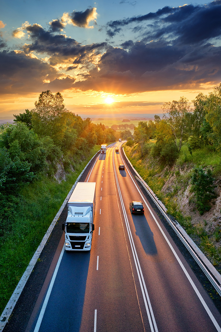 Cars and trucks drive on a three-lane road.