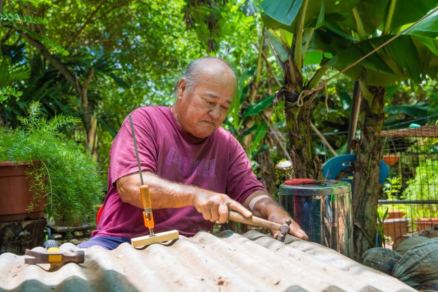 Abraham Taimanao hammers two sheets of tin to make a roof for the chicken coop he is building.