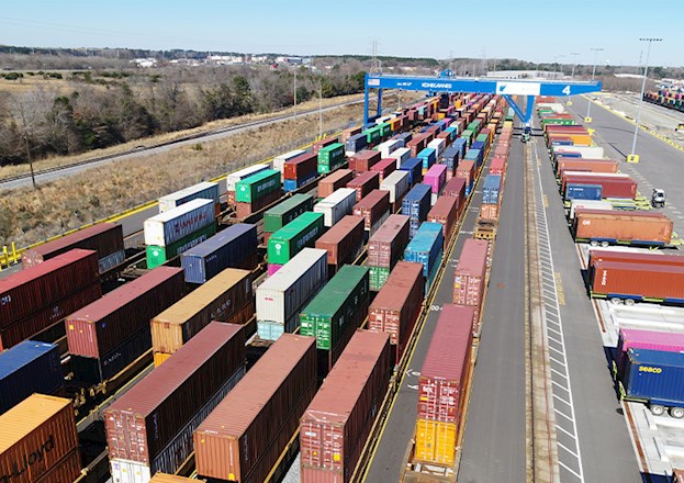 Multiple shipping containers in different colors sit in a shipping yard. 